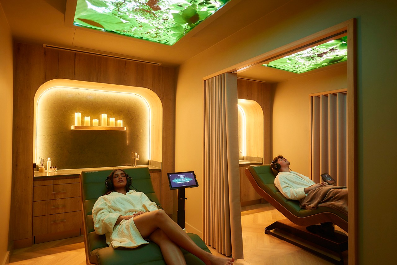 Man and women standing and sitting in a calmly lit area with comfortable seating.