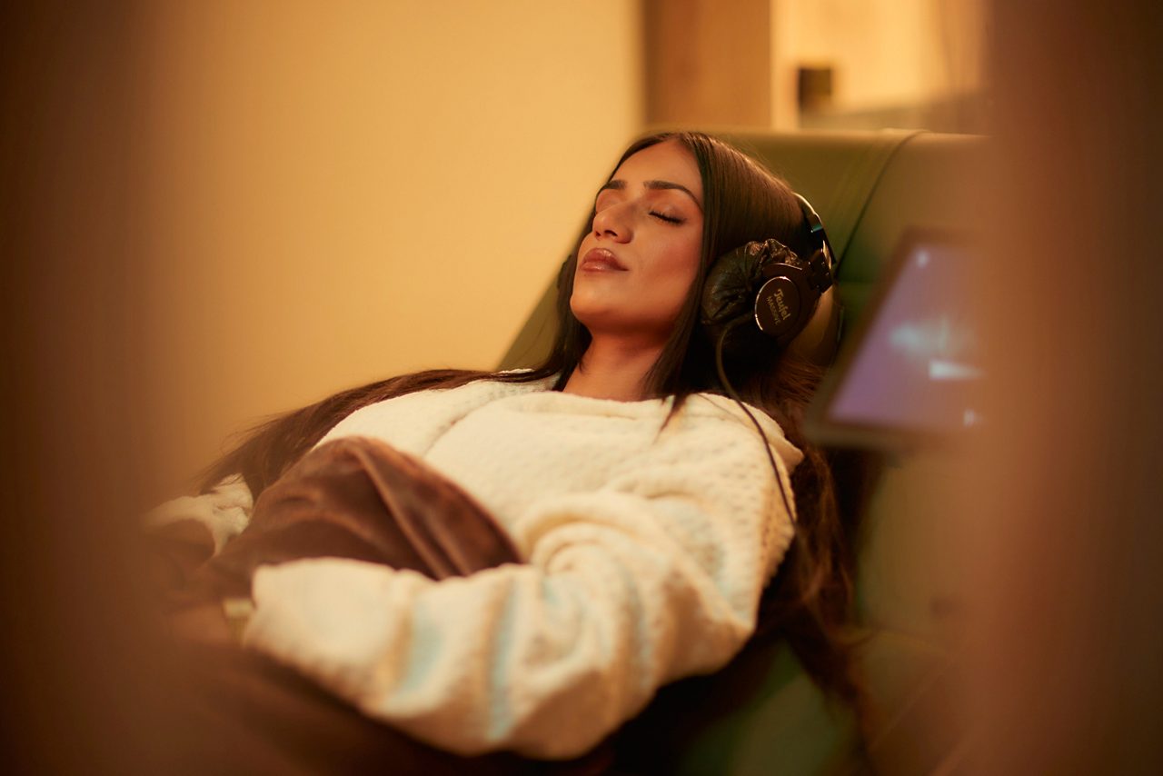 Woman laid back wearing a fluffy spa robe and headphones.