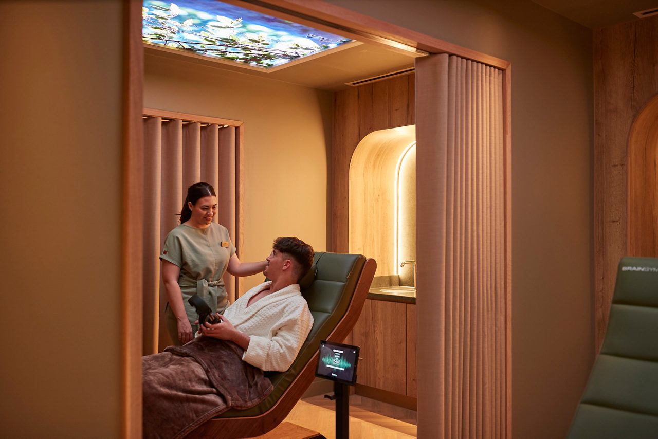 Spa therapist talking with a man as he reclines in a comfortable chair.
