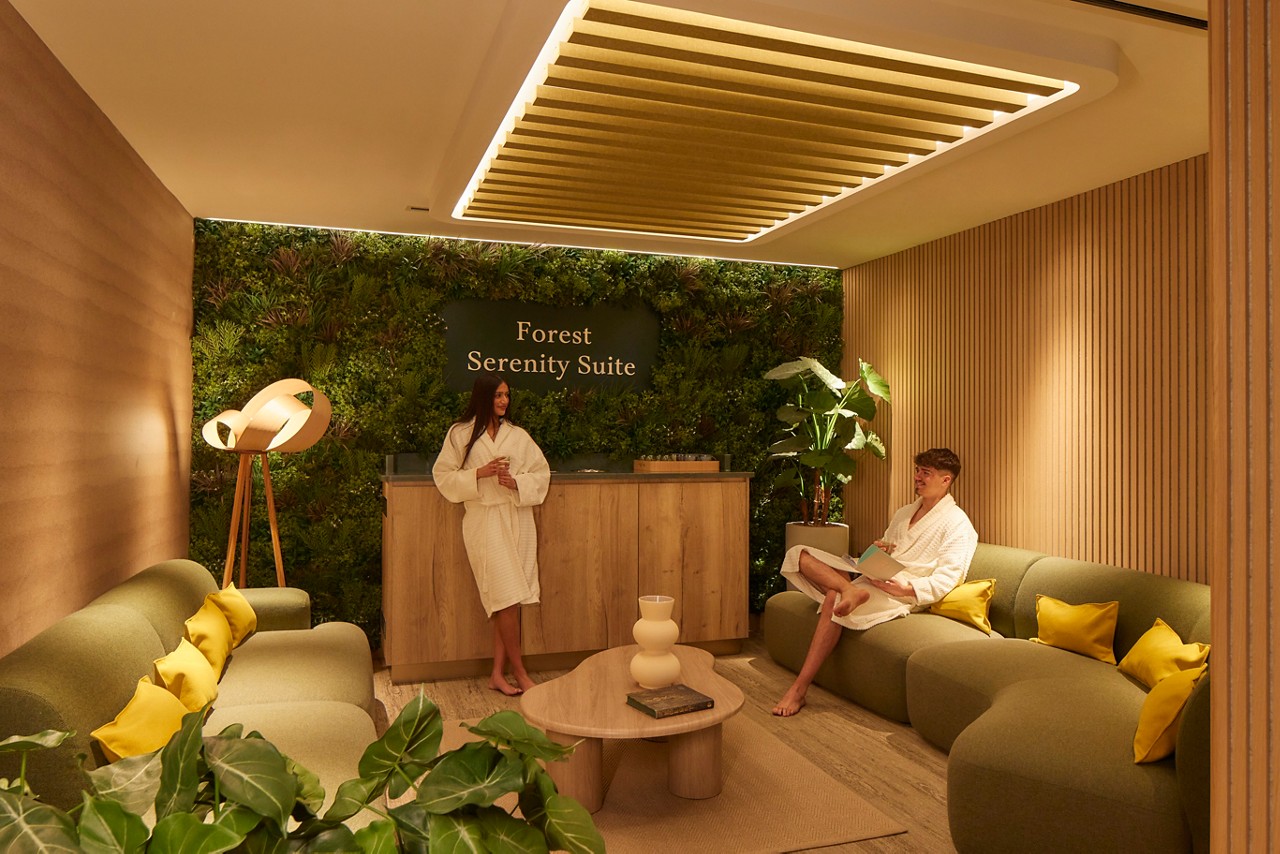 Man and women standing and sitting in a calmly lit area with comfortable seating.