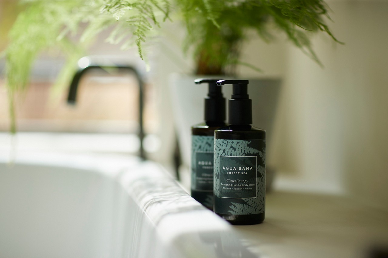 hand & body lotion and hand & body wash bottles in black and green sat on side next to a bath 