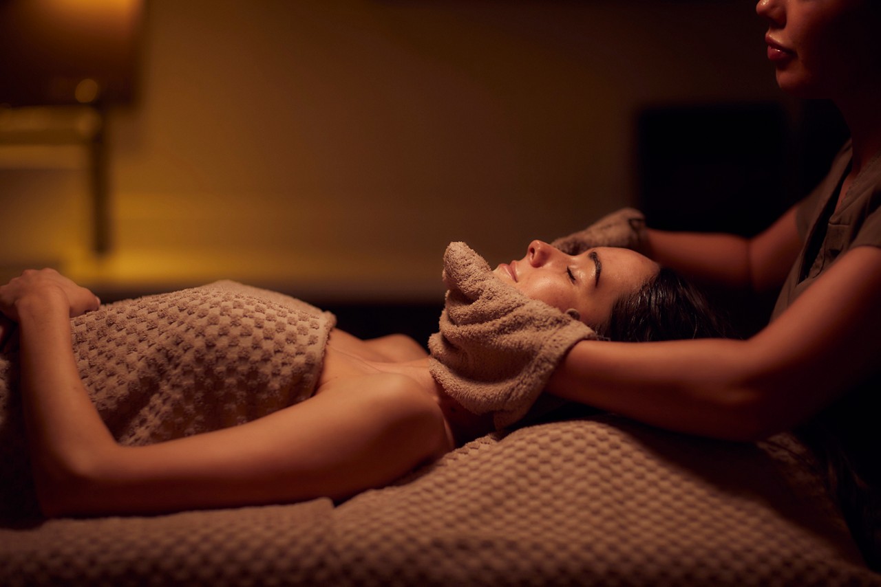 Spa therapist giving a woman a warm towel facial treatment.
