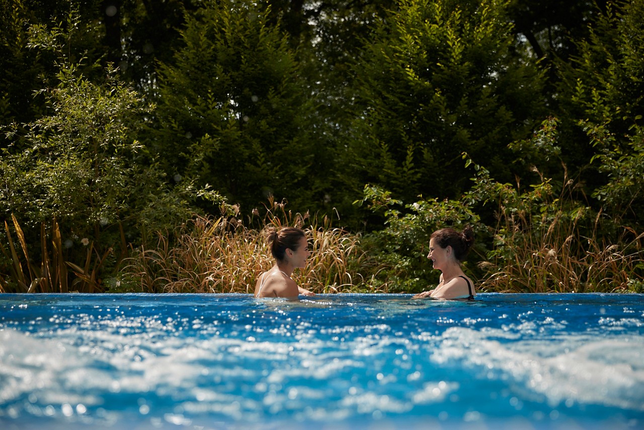 Two ladies spending time together as they soak in an Outdoor Pool surrounded by the forest.