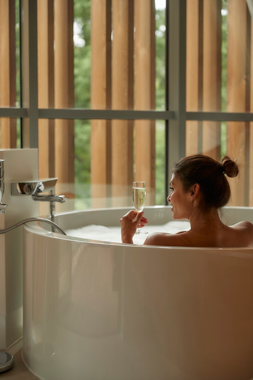 Woman sipping champagne as she soaks in a bubble bath.