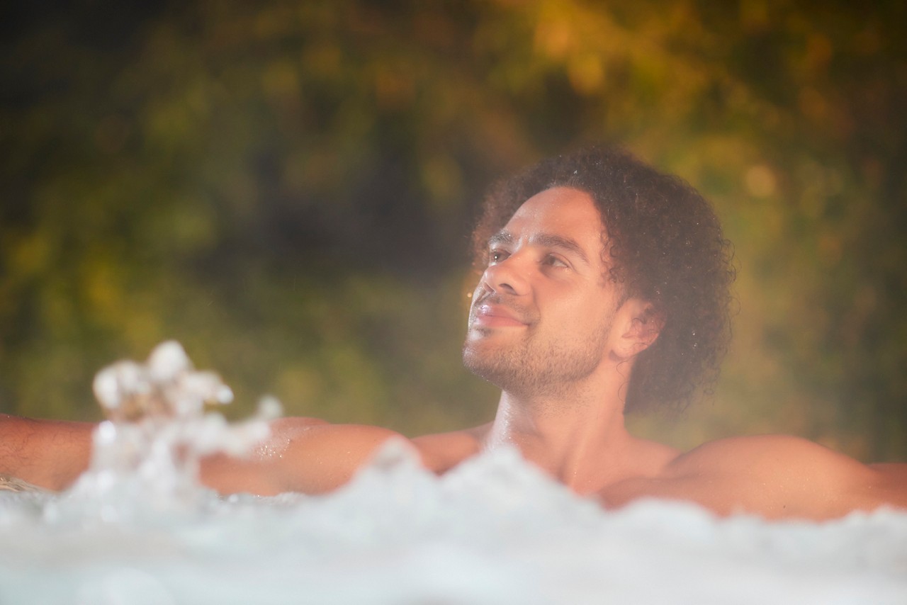 A man soaking in a steamy outdoor hot tub.