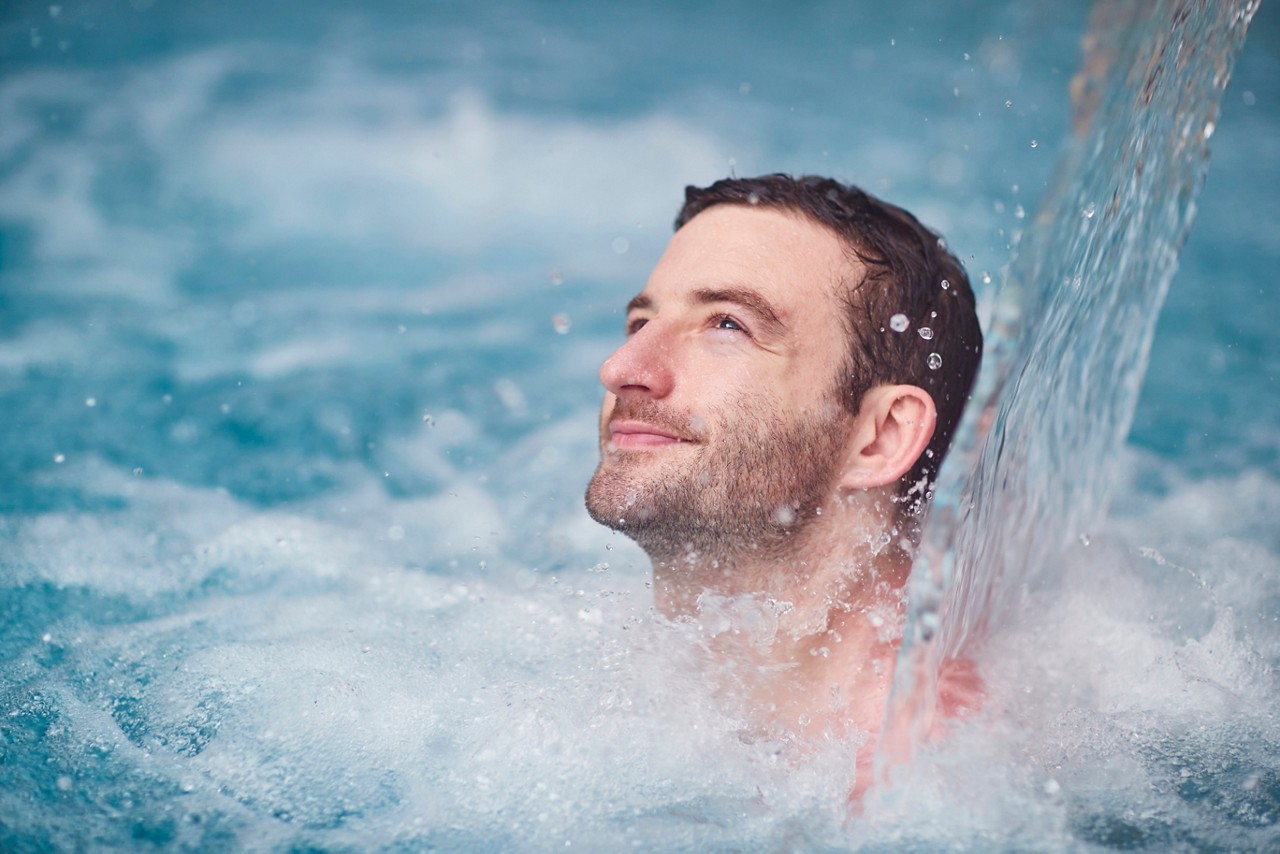 Man soaking under a flowing water fountain.