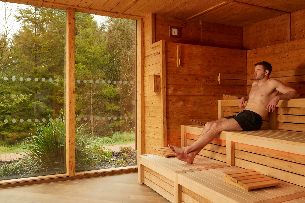 Woman sitting in a Nordic Sauna looking out to the forest.
