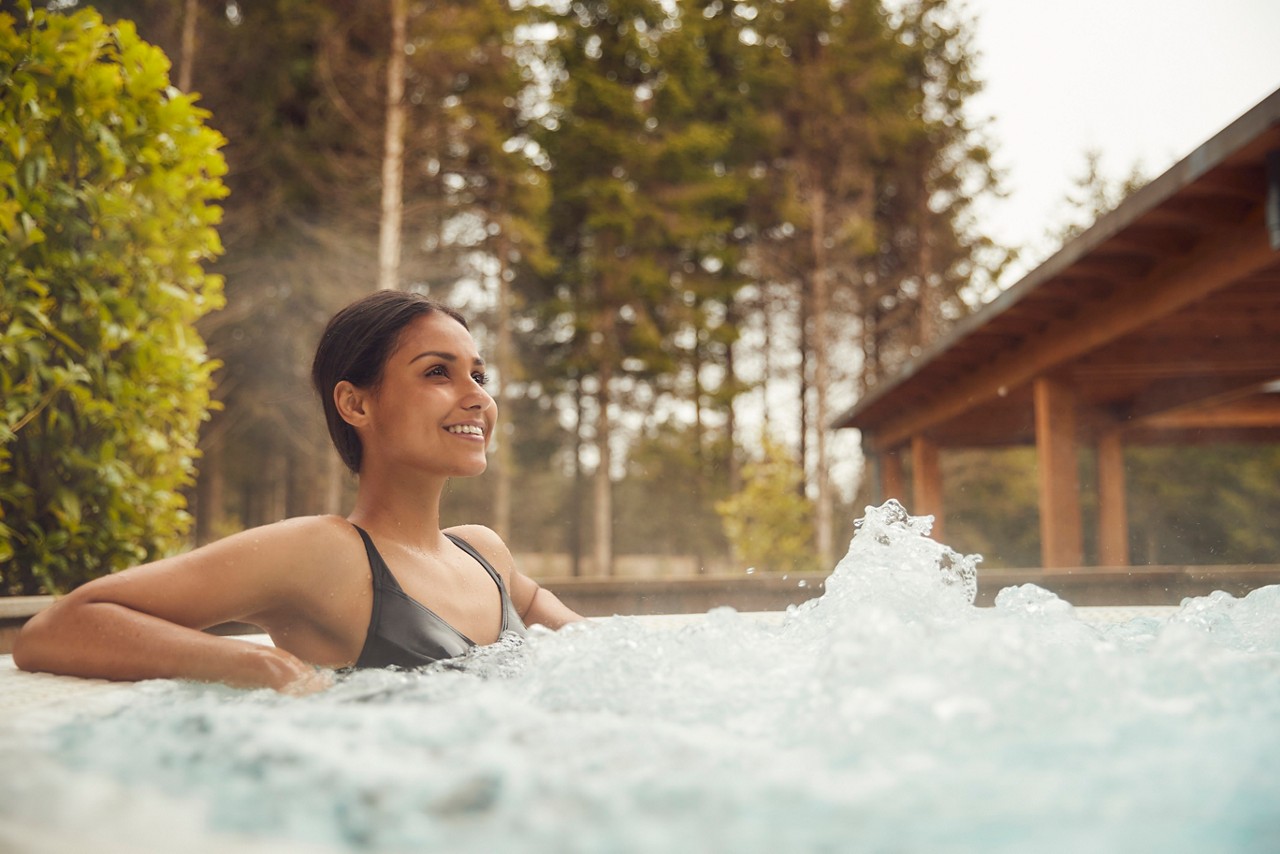 Woman soaking in a bubbling hot tub surrounded by the forest.