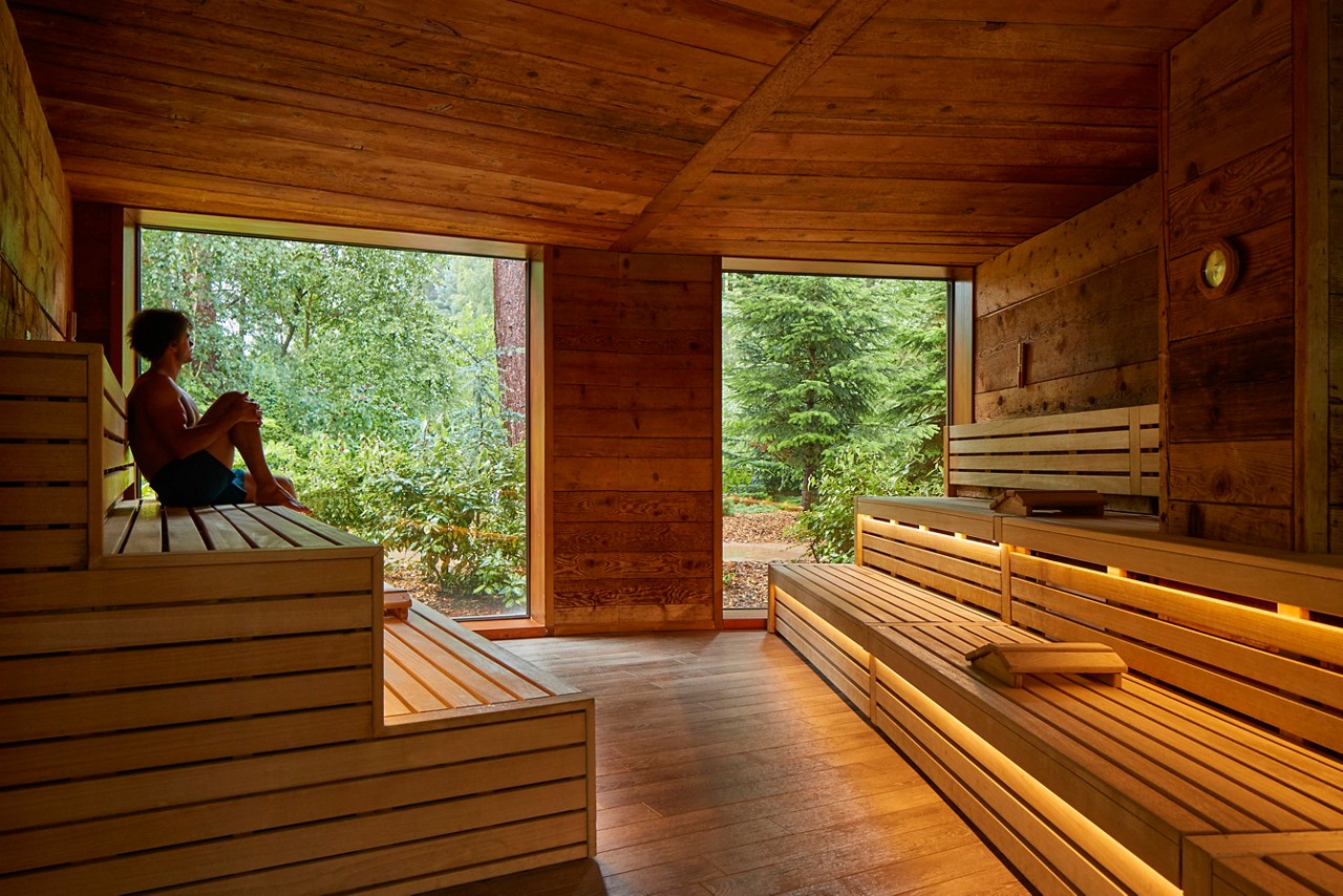 Man sitting inside a wooden Nordic Sauna with forest views.