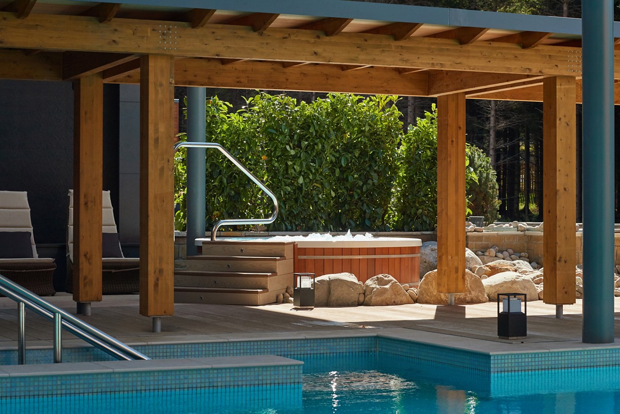 Bubbling hot tub under a Pergoda beside and an outdoor pool.