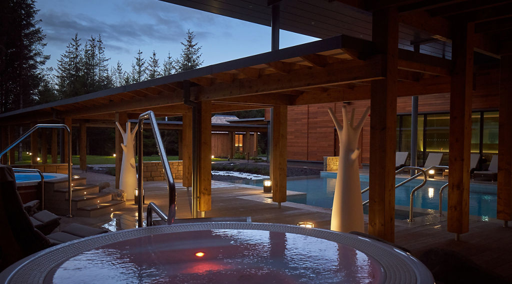 Woman soaking in an outdoor pool surrounded by the forest.