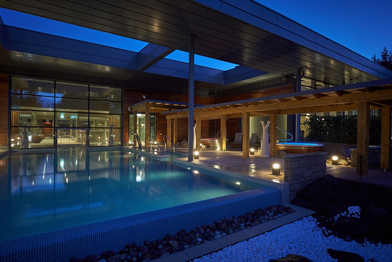 Outdoor pool in the evening with a pergola lit by outdoor lighting.