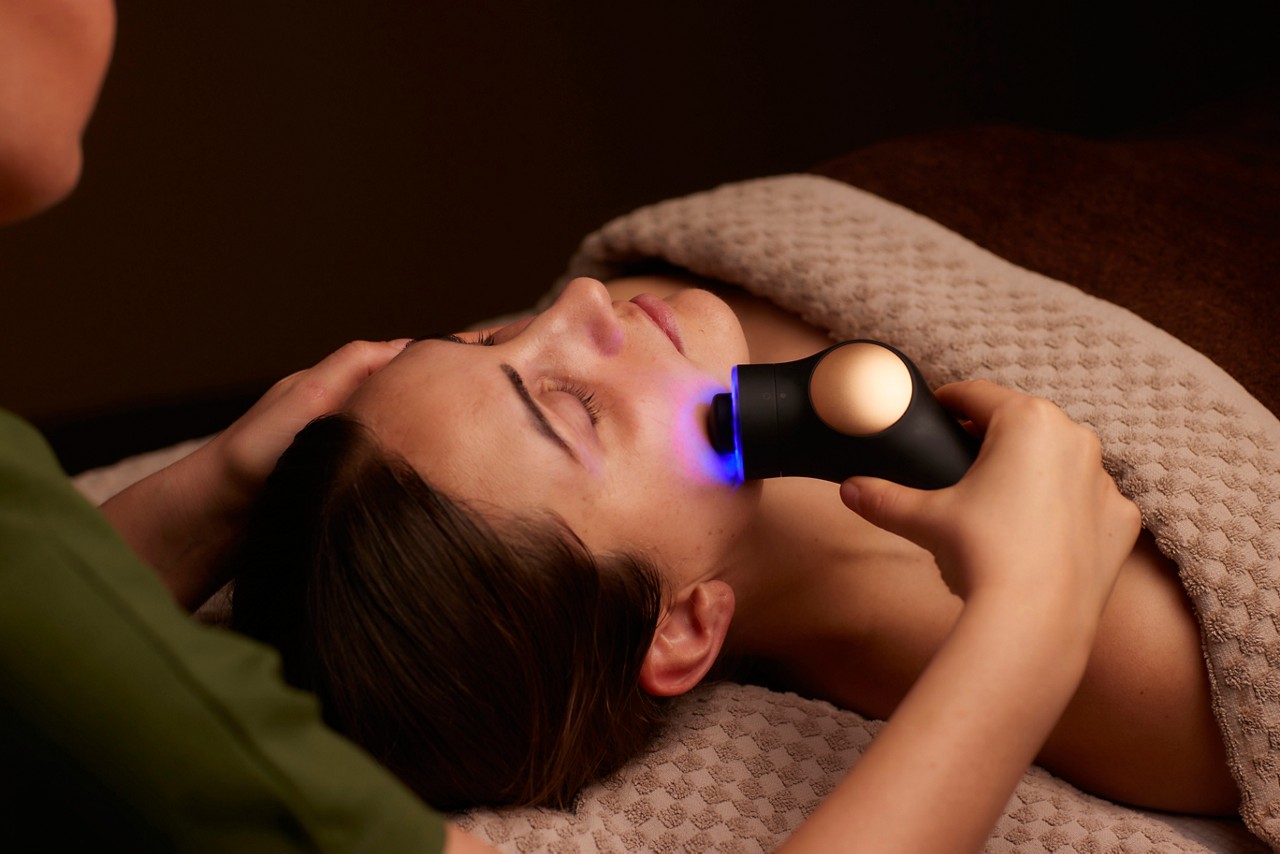 Spa therapist giving a woman a Theraface microcurrent facial treatment.