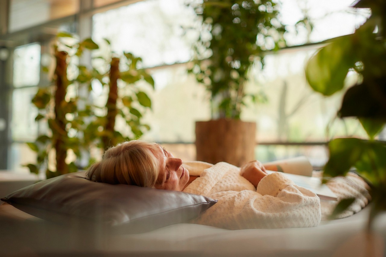 Lady laid back on a Waterbed in a serene area with lots of plants and natural lighting.