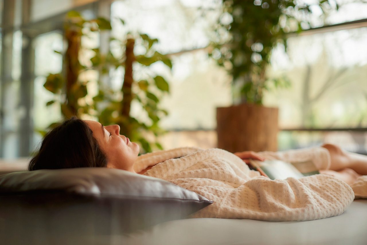 Woman laid on a Waterbed in a serene area with lots of plants and natural light.