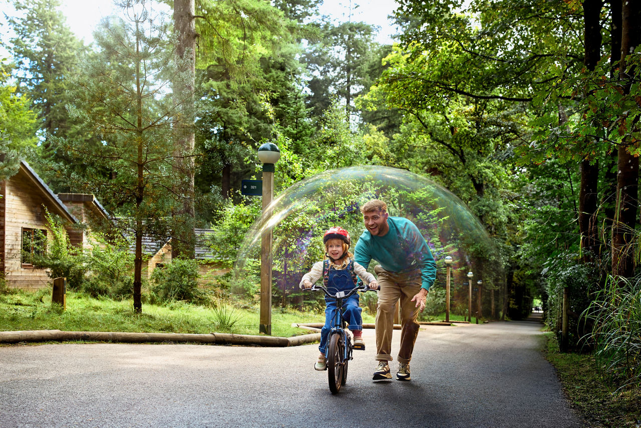A father helping his child learn to ride a bike in the forest.