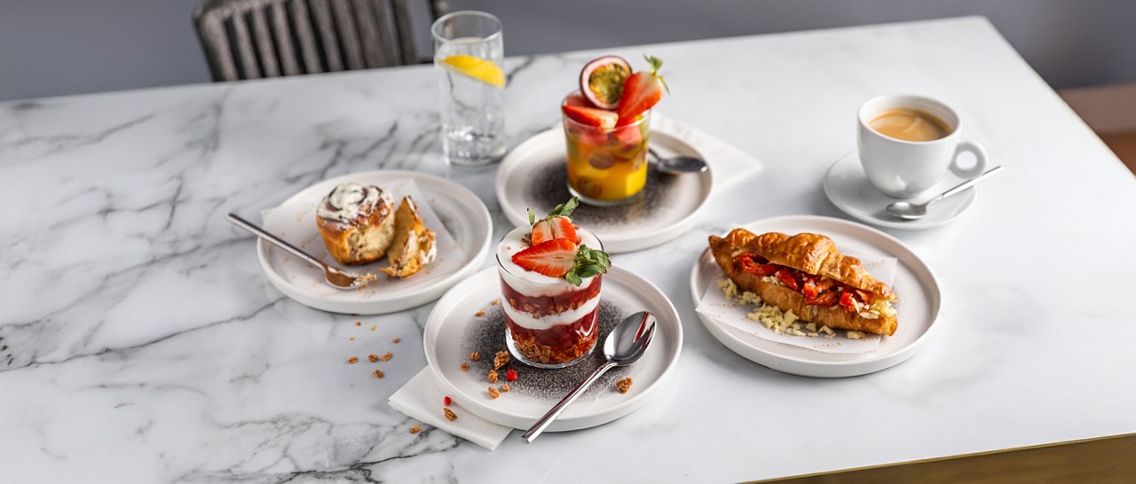 A selection of breakfast dishes, including yogurt with granola, stuffed croissant and fruit salad.