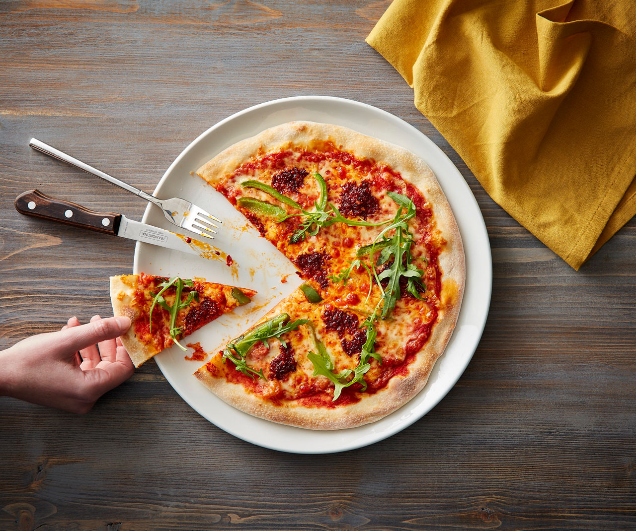 A hand taking a slice of pizza from a white plate