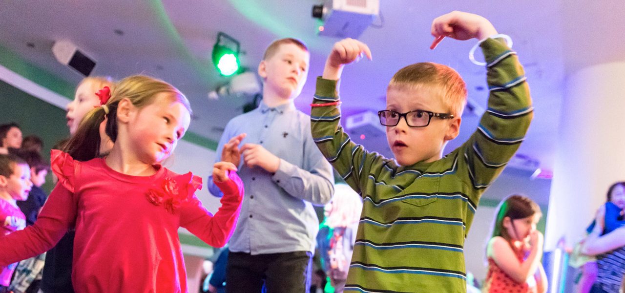 children at a disco with their arms in the air dancing