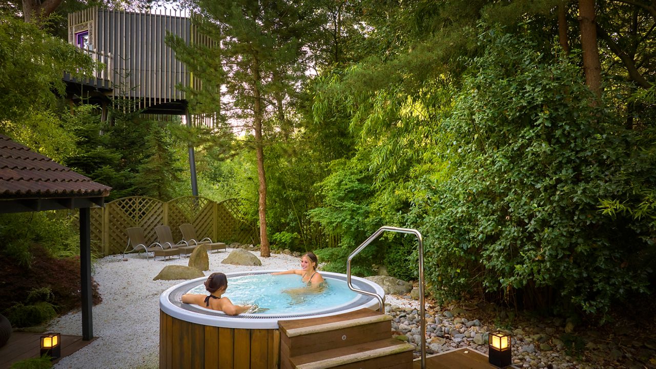 Two people soaking in an outdoor hot tub surrounded by the forest.