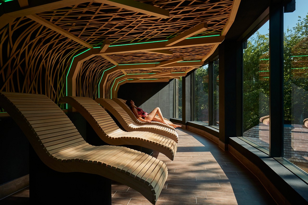 Woman lounging on a contoured wooden seat, looking out at panoramic views of the forest.
