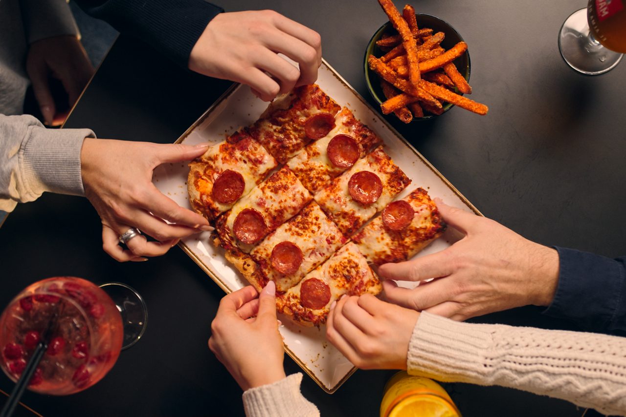 Hands diving in to a pepperoni pizza. 