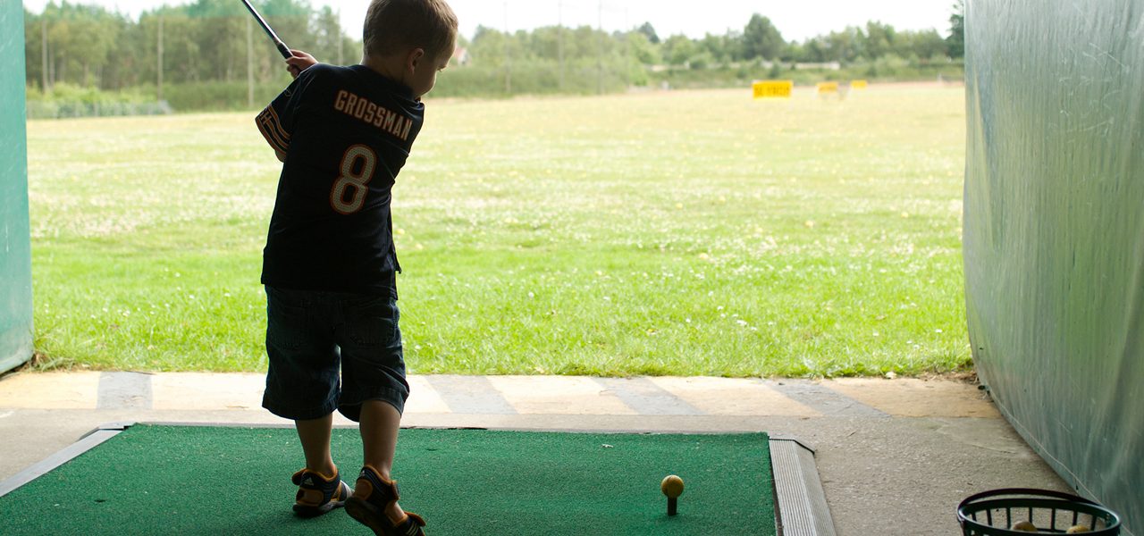Child golfer swings a club at a yellow-teed ball on a practice mat