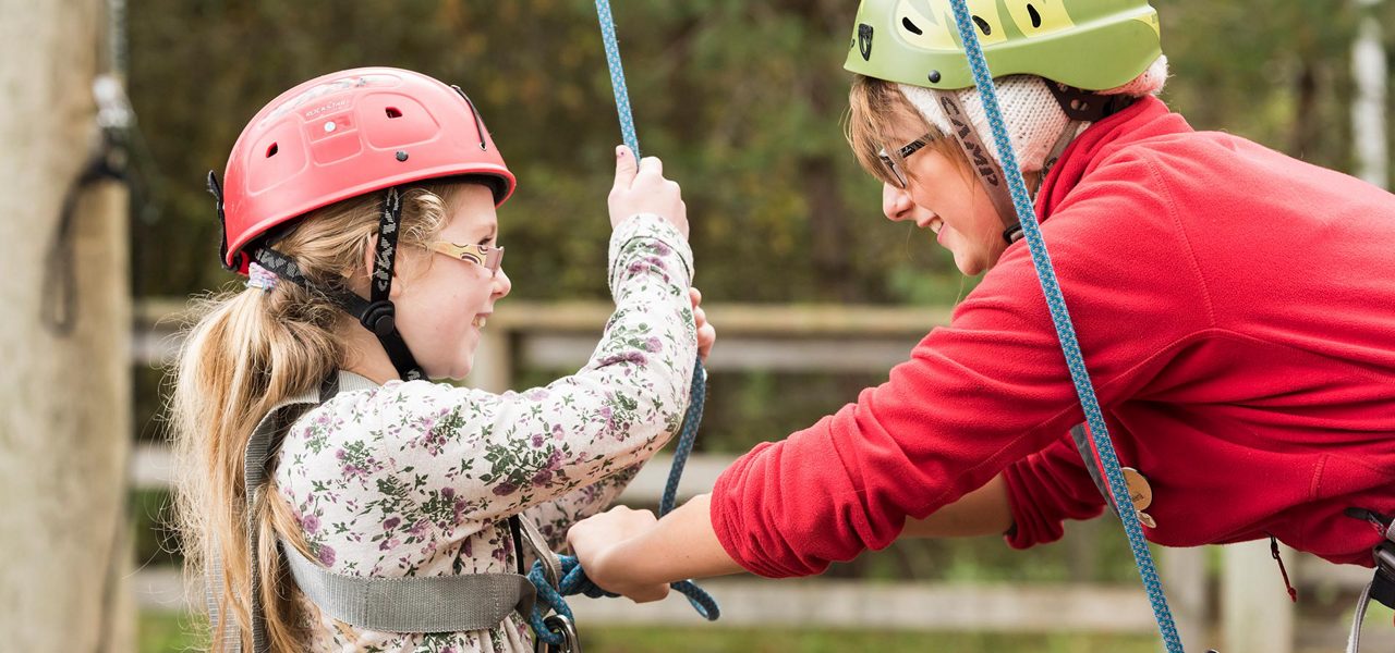 member of staff fastening a child's harness for the high ropes