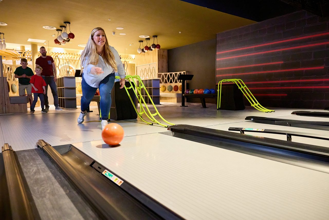 Woman bowling a ball down a bowling alley lane.