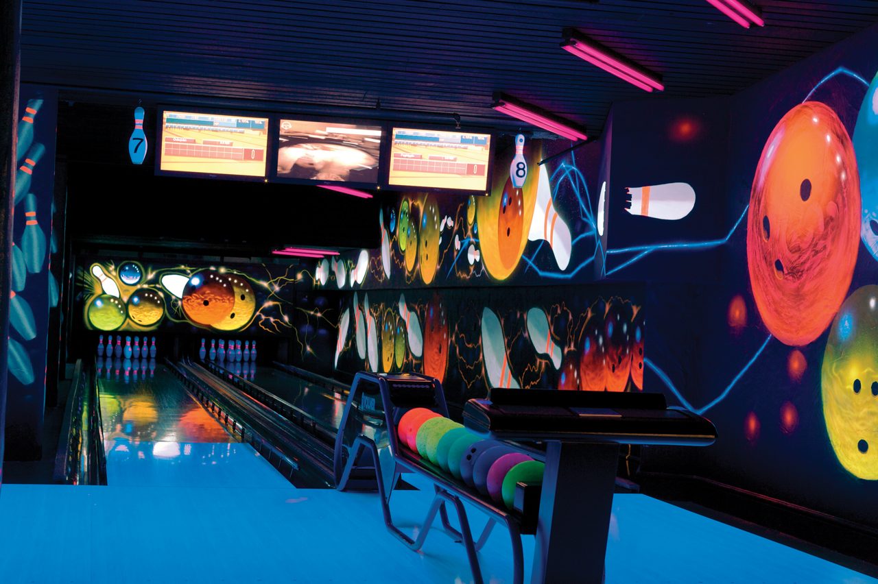 Neon lit bowling alley with colourful balls lined up.
