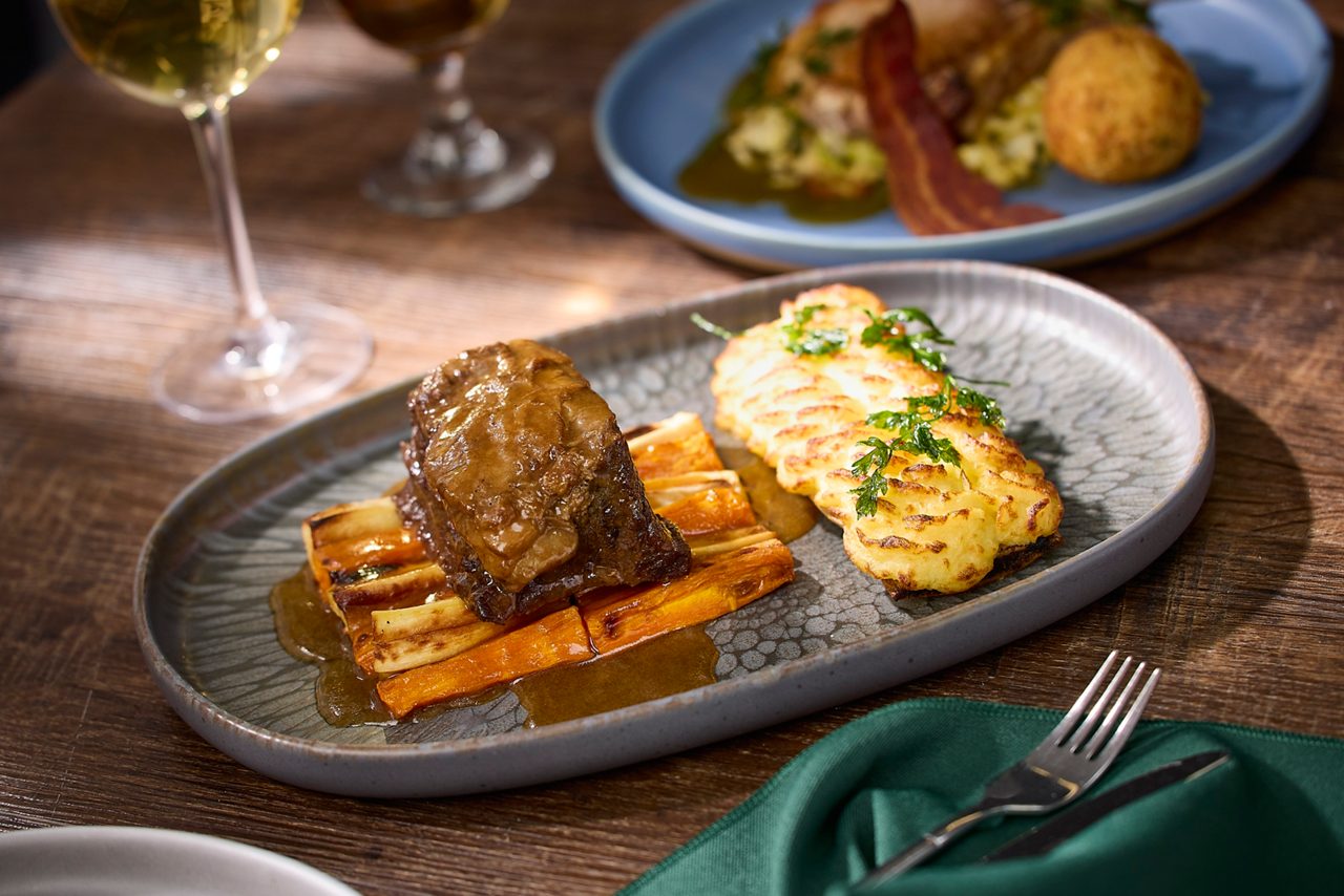 Restaurant meal on a grey plate on a wooden table with another meal behind on a blue plate and a fork on a green napkin