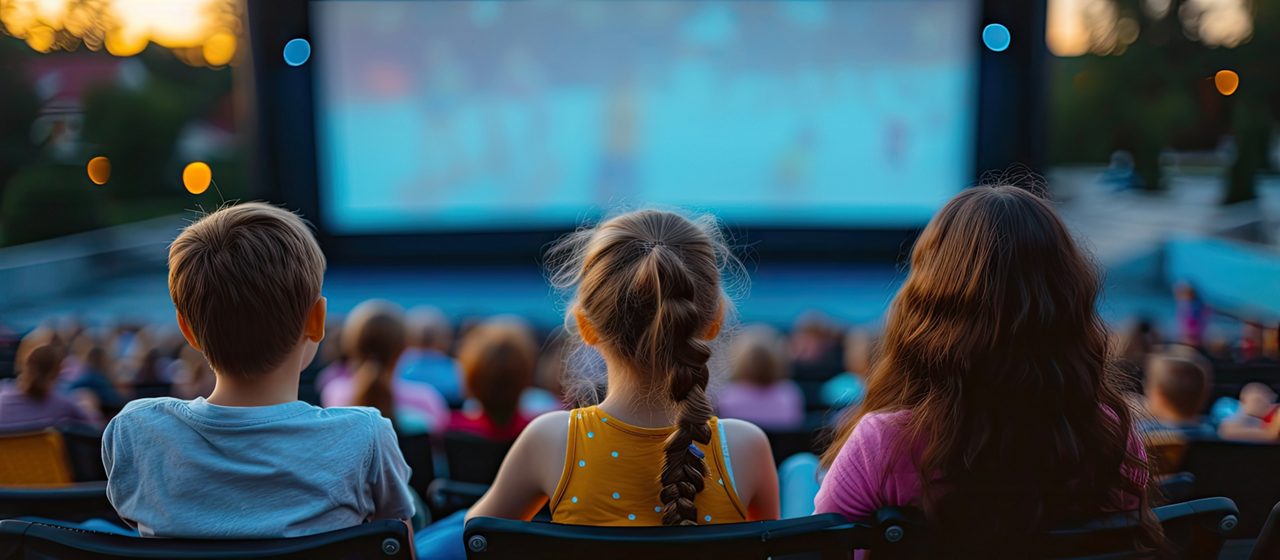 Children sat watching a film on an outdoor cinema.