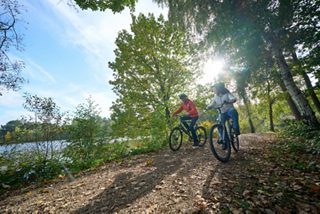 Brother and sister cycling in the forest together.