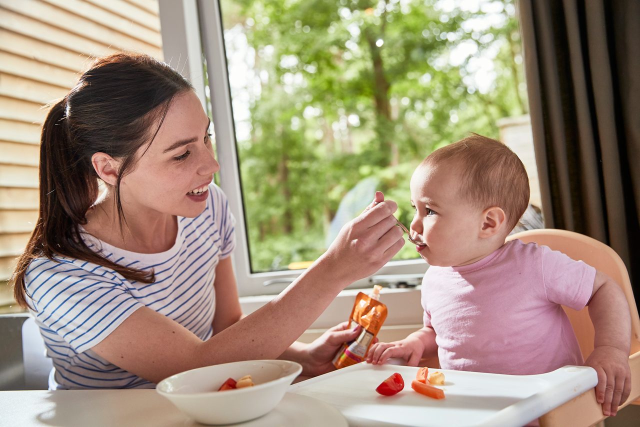 A mother feeding her child in a highchair in their lodge.