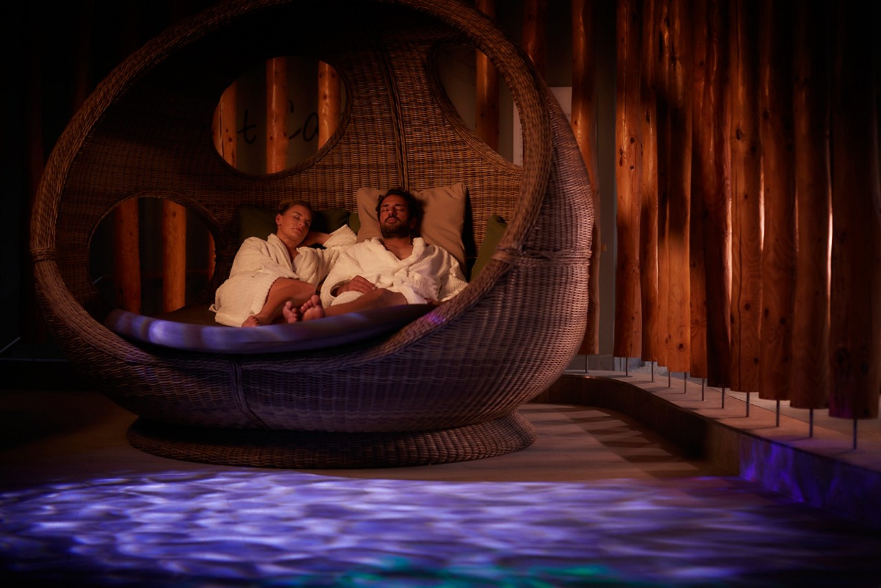 Couple snuggled in a large, cosy cocoon chair in the Forest Nesting area.
