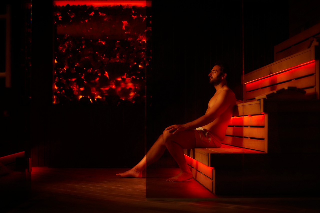Man sitting inside a Lava Sauna with a glowing coal wall.