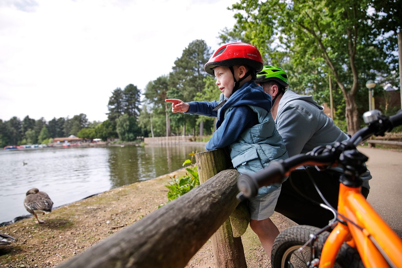 young boy in helmet looking out over the lake, him and his dad both have bikes next to them