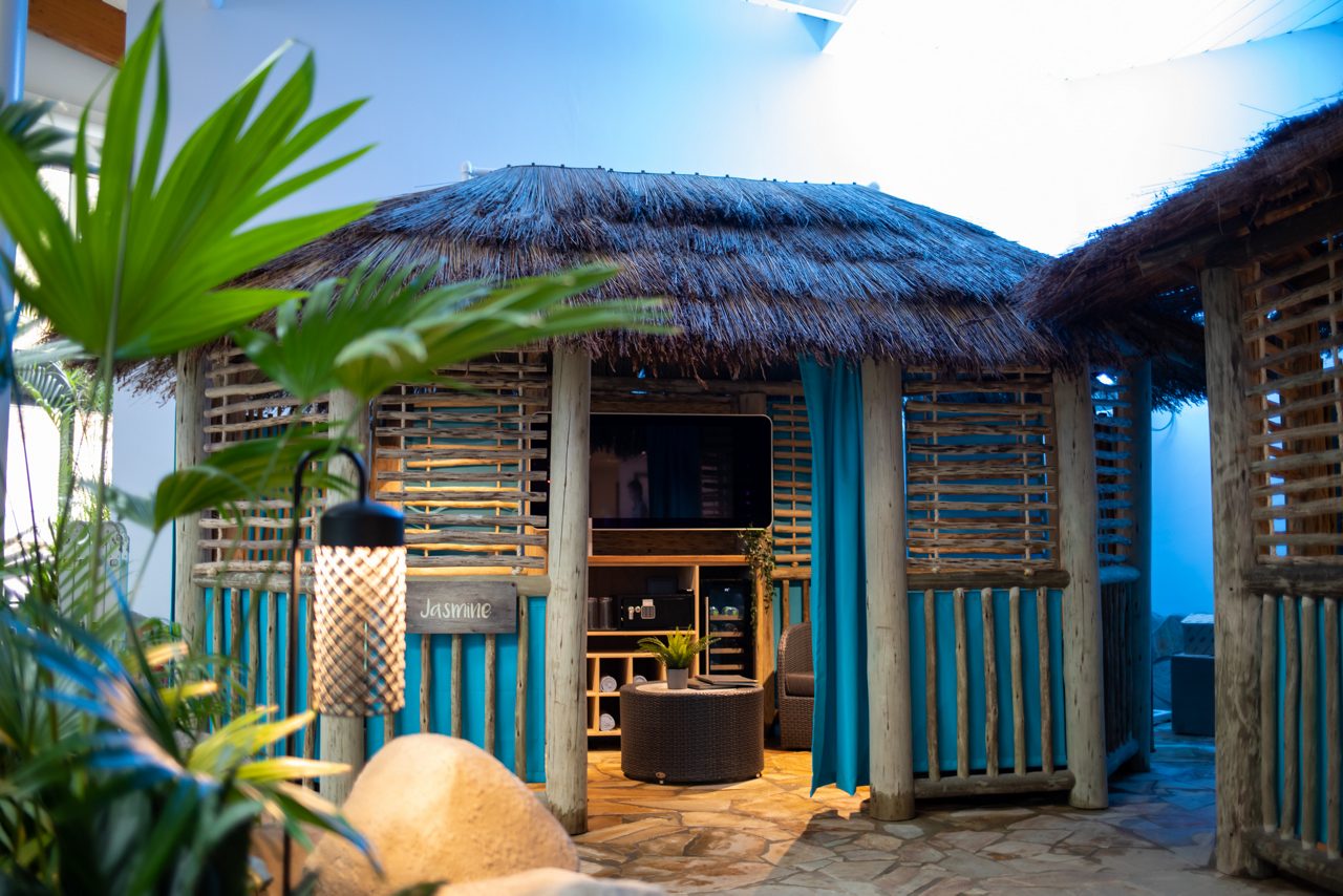 Inside a Cabana with seating, a wall mounted TV and fluffy towels.