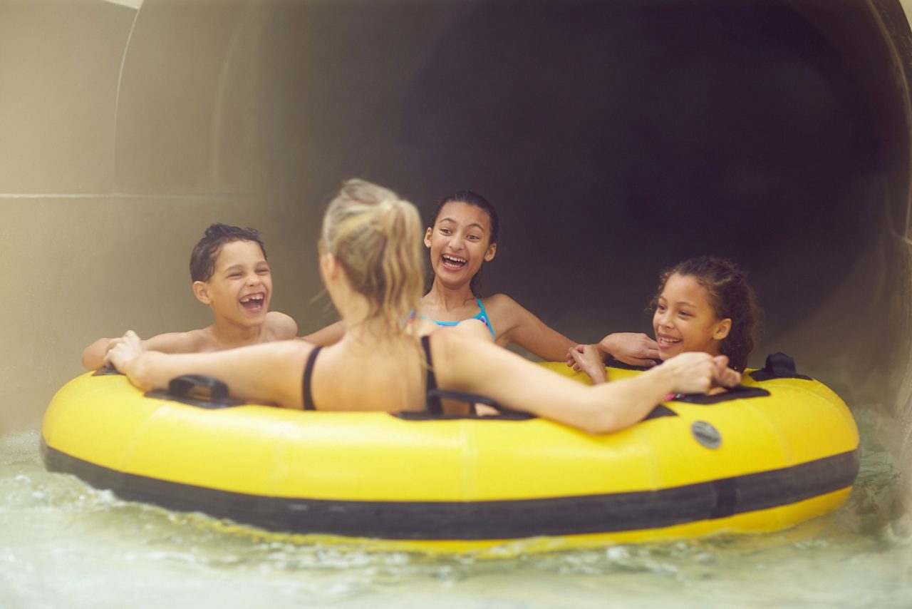 Family sitting in an inflatable raft, heading down a dark water slide.