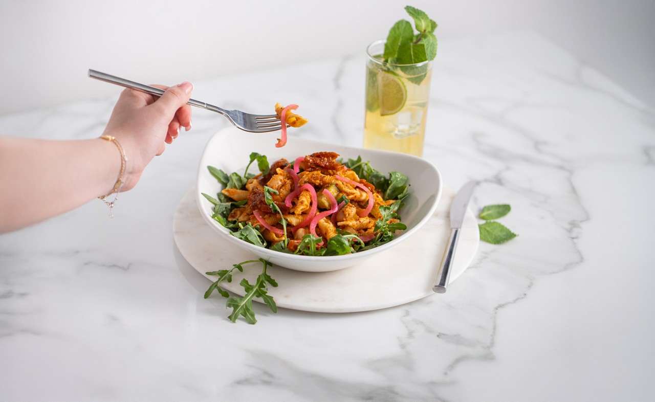 and hand with a food taking food out of a white bowl filled with a salad dish
