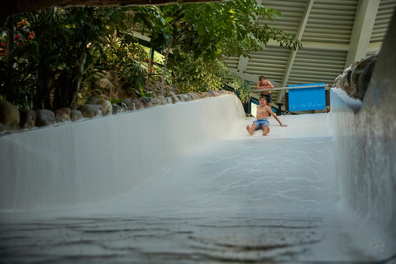 Two people with their arms spread as they slide down a near vertical water slide.