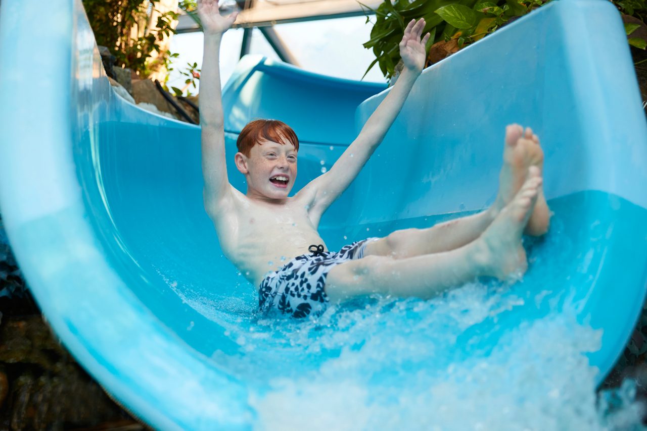 Young boy with his arms in the air as he splashes down a flume.