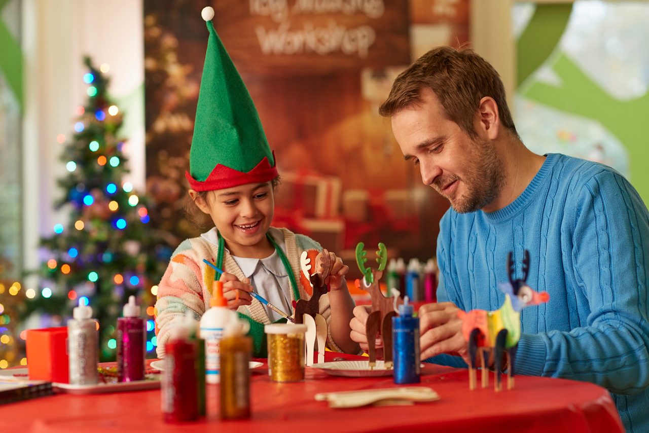 Girl sat with an adult painting wooden reindeer.