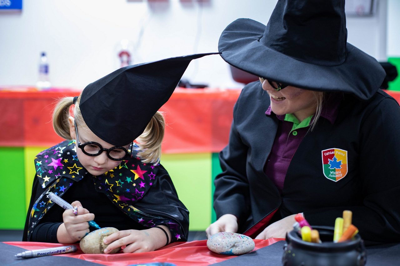 A little girl dressed as a wizard and painting rocks.