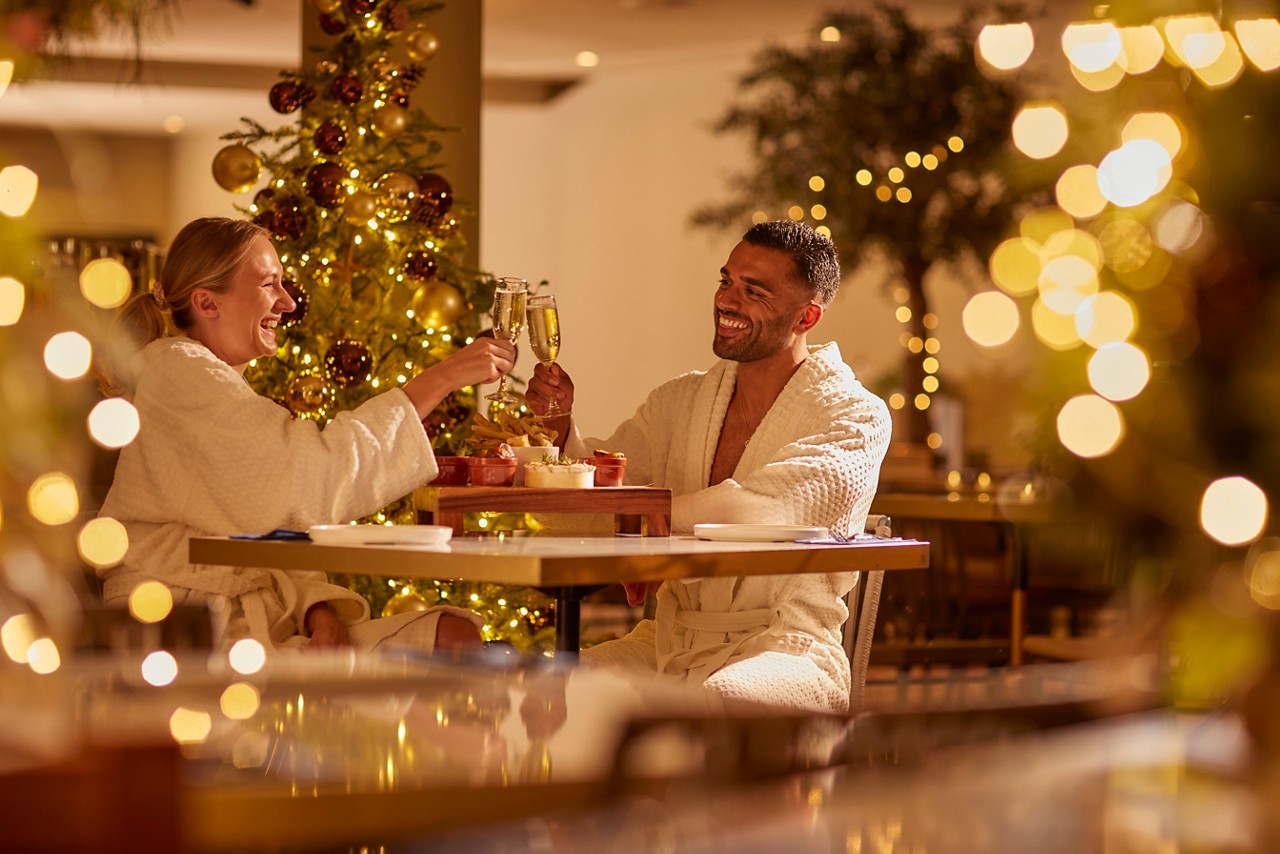 Two people sat at a table in spa robes with prosecco