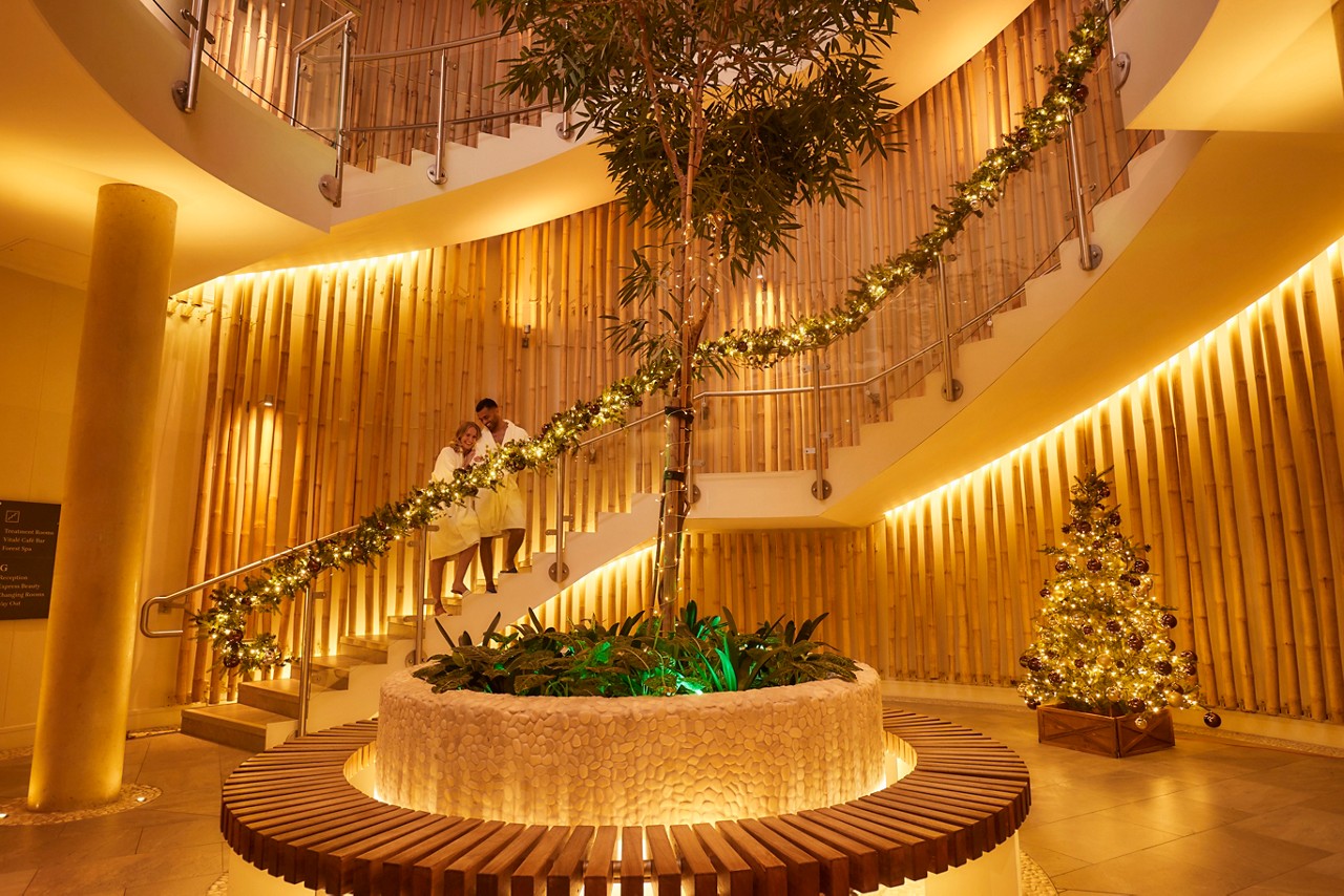 Two people in spa robes on spiral staircase that is covered in scristmas wreath decorations