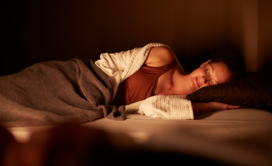 Woman snuggled under a cosy blanket in a dim lit room.