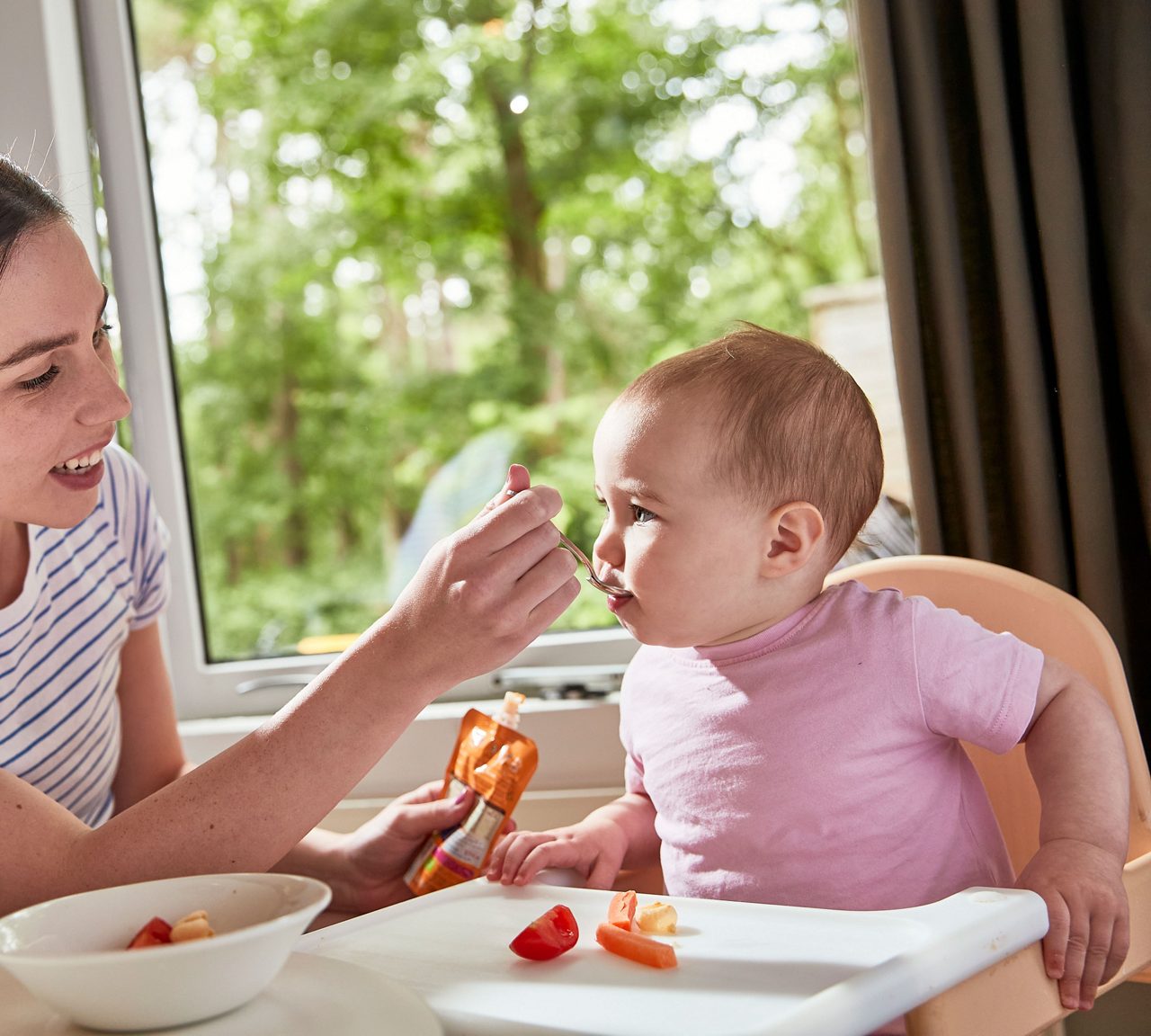Woman feeding a baby a Ella's Kitchen pouch.