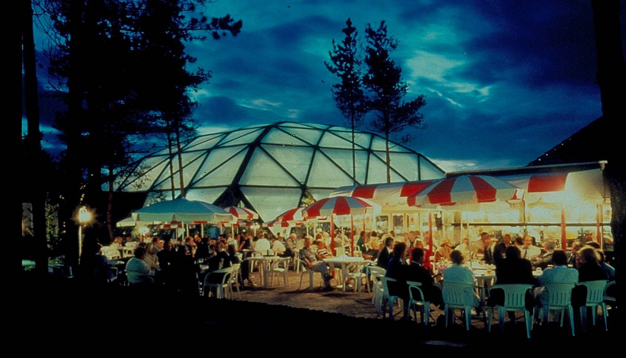 People wearing evening attire sat at tables outside at night time 