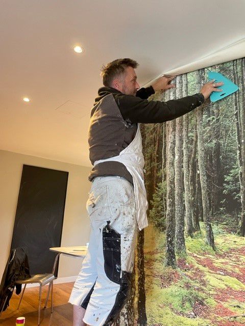 A man in an apron putting up wallpaper in a lodge